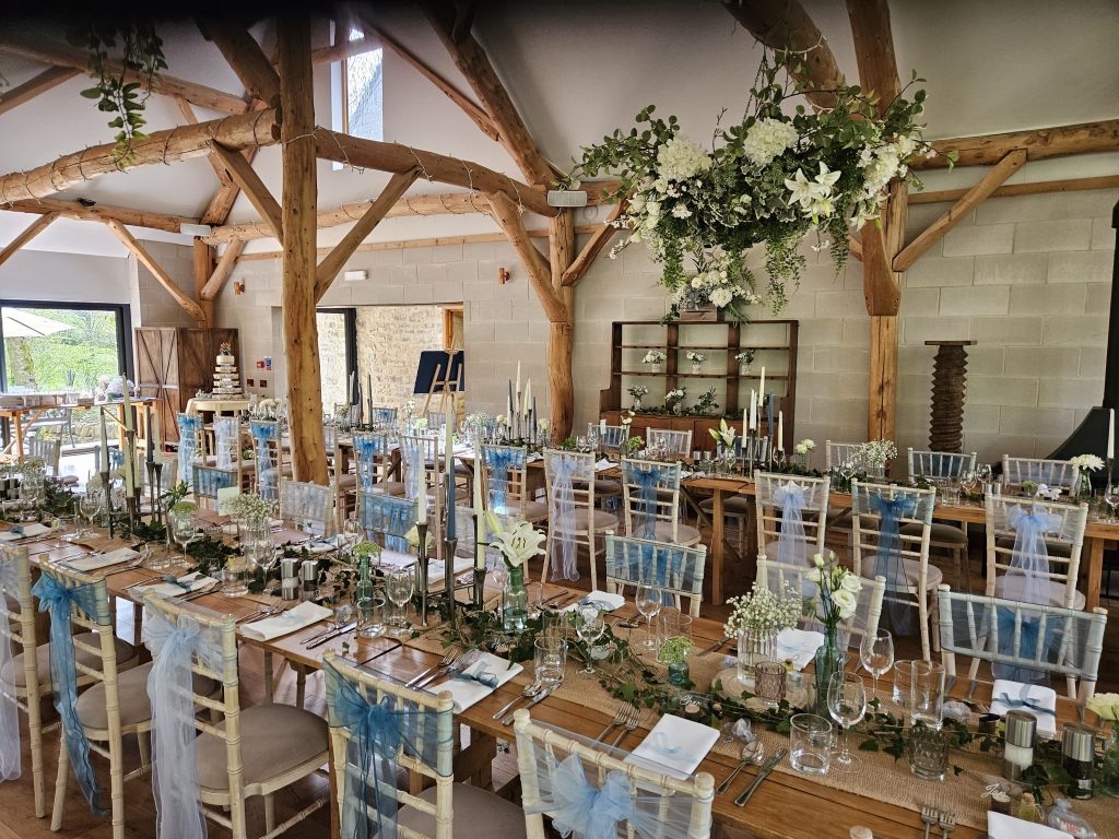 Trestle tables at owlpen manor, with hessian runners down the middle of each table. with ivy twisting around aqua bottles, slices of wood with jars filled with gypsophila on top and gothic style seven spoke candelabras